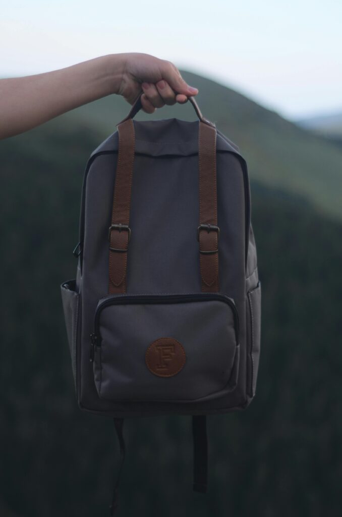 Inicio A person holding a stylish gray backpack with leather straps, set against a natural outdoor background.